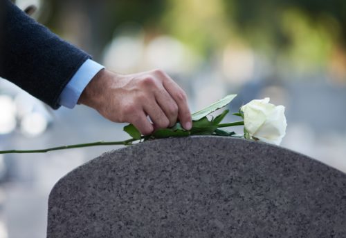 man-placing-white-flower-on-gravestone
